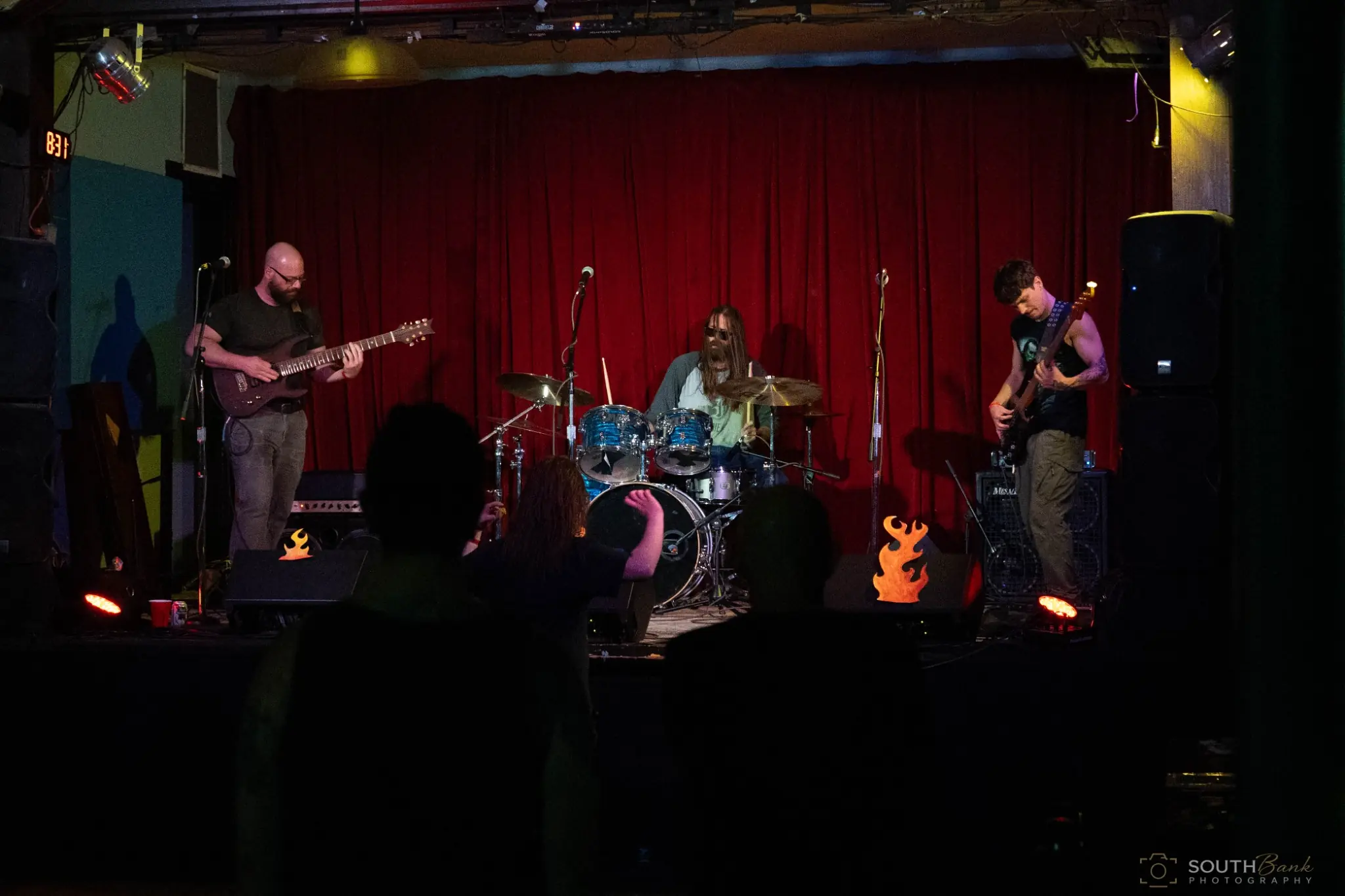 Rock trio performing before a deep red curtain