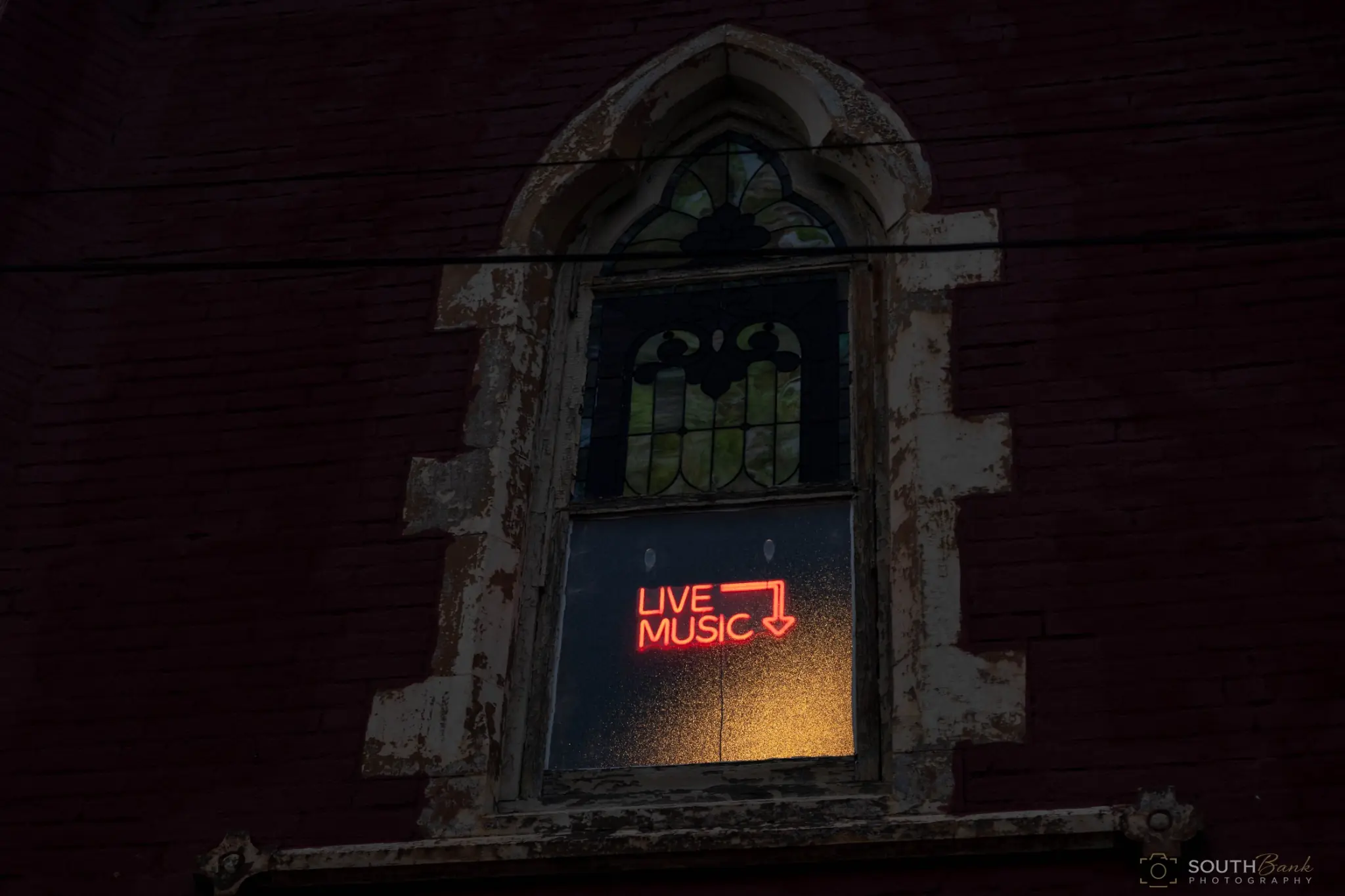 Live music sign glowing in a weathered arched window after dark