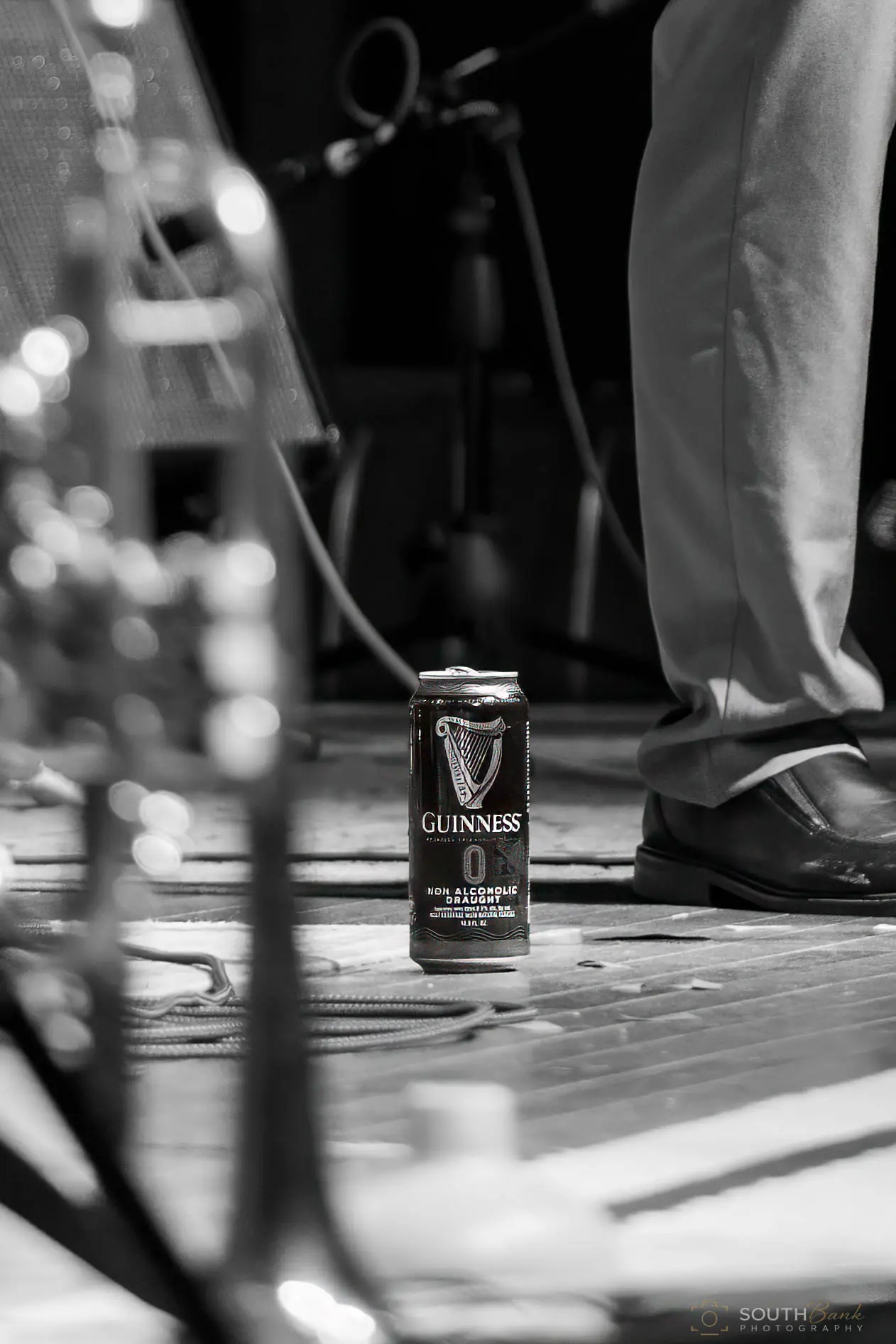 A beverage can and musician's feet photographed at stage level in black and white